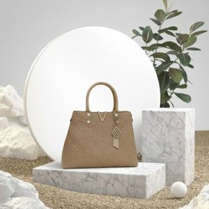Gold textured women’s tote handbag with top handles and elegant charm detailing placed on a white fur surface.