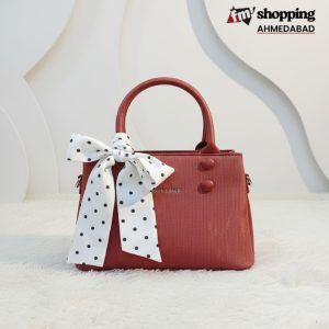 Ruby red velvet-textured handbag with button detailing and a white polka-dot scarf tied on the handle.